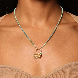 Boho turquoise beaded necklace with gold sun pendant worn on a cozy knit sweater