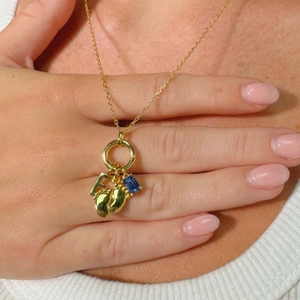 Detalle de cadena de oro 18K con colgante letra F, zafiro y dijes de pies de bebé