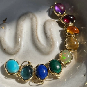 Regenboog edelsteen hangers met 18K goudlaag en ovale natuurstenen op een keramisch bord