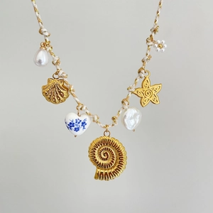 Detail of knotted rope necklace featuring gold seashells, pearls, and ceramic heart pendants