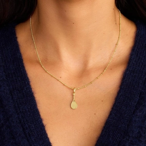 Makro-Detail des goldenen Tennisschläger-Anhängers mit Perlenkette auf blauem Pulli
