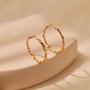 Macro detail of large gold hoop earrings with geometric diamond-cut faceted texture
