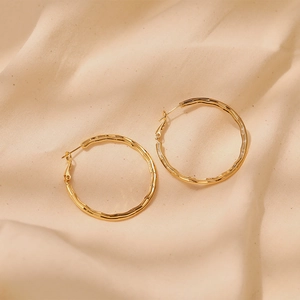 Detailed view of large gold hoop earrings with unique bamboo texture on beige fabric