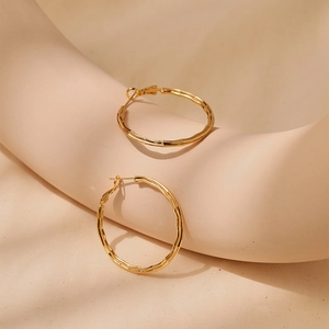 Detailed view of textured 18K gold plated hoop earrings on minimalist background