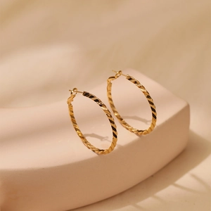 Macro shot of gold hoop earrings featuring twisted texture and light-reflecting details