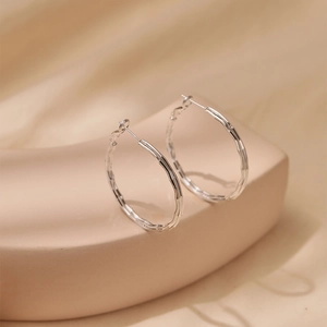 Detailed close-up of silver-tone hoop earrings with wave texture on a minimalist display