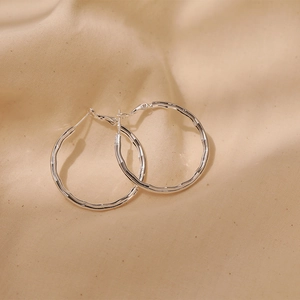 Minimalist S925 silver hoop earrings with a textured wavy surface on beige linen