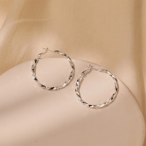 Macro shot of silver textured hoop earrings with a twisted lattice pattern on a display