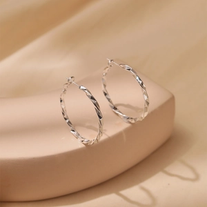 Macro view of twisted faceted silver hoop earrings showing light reflection on metal