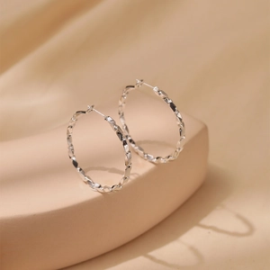 Close-up of silver-tone large hoop earrings featuring faceted texture and S925 needles