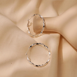 Close-up of silver hoop earrings with faceted geometric texture on fabric background