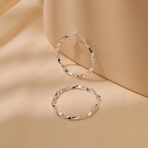 Close-up of twisted texture silver hoop earrings with irregular wave metallic facets