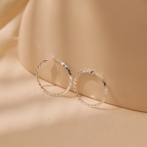 Close-up of silver hoop earrings with twisted faceted texture on beige background