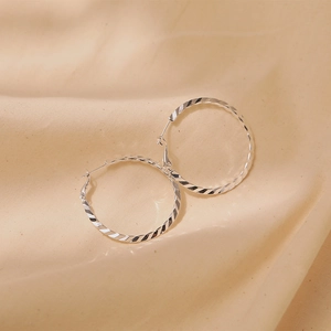 Detail of silver twisted hoop earrings with spiral cut texture on silk background