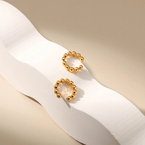 Detail of minimalist gold beaded ear cuffs displayed on a white textured stand