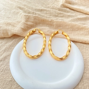 Makro-Detail von großen 18K vergoldeten Spiral-Ohrringen auf einem weißen Teller