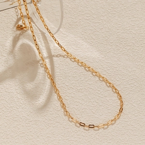 Detalle de la cadena de clips bañada en oro pulido sobre una superficie de piedra texturizada