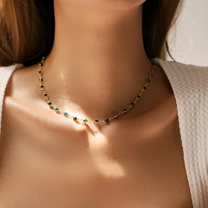 Dettaglio di una collana a margherita dorata con perle verdi e nere sulla clavicola