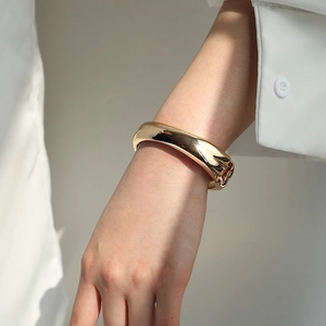 Polished gold wide bangle bracelet with side clasp shown on a model wrist with soft shadows