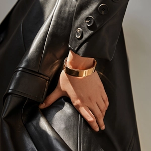 Macro detail of wide gold hinged bracelet with mirror finish on black leather sleeve