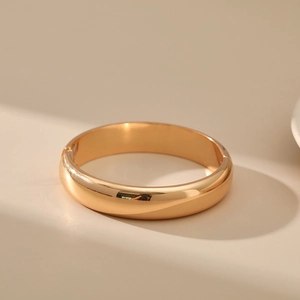 Close-up of minimalist wide gold-plated bangle with mirror-polished finish and hinge clasp