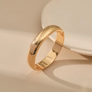 Macro detail of gold-plated metal bangle showing polished finish and hinge closure