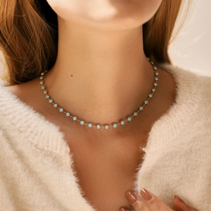 Dettaglio della collana con perline blu e catena dorata su un maglione beige