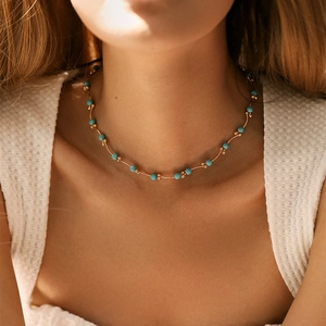 Collana boho con perline turchesi e tubi dorati indossata su top bianco con texture