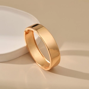 Close-up of golden minimalist glossy bangle with a hinged opening on a display stand