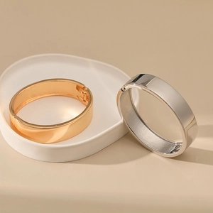 Macro detail of minimalist wide polished gold and silver bangles with hinge closure