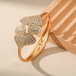 Detailed close-up of gold heart-shaped bracelet with pave-set rhinestones on a wooden stand