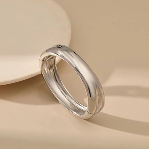 Close-up of polished silver wide hinged bangle with glossy mirror finish on beige surface