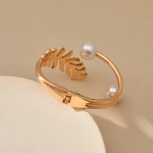Detail of golden leaf bracelet with white pearl accents on minimalist display stand