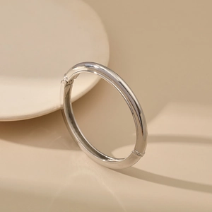 Polished silver metal bangle with hinge closure on elegant beige background