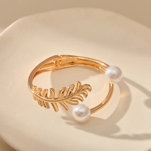 Macro detail of golden leaf-shaped bangle featuring twin pearl accents and hinged closure