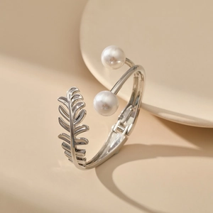 Macro shot of silver metal bangle featuring white pearls and detailed leaf engraving