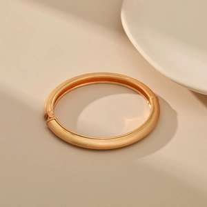Close-up of a matte gold minimalist bangle featuring a textured brushed finish with a hinge