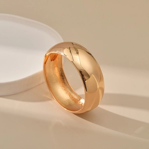 Detail shot of wide minimalist golden bangle with smooth polished metallic finish
