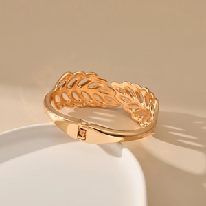 Detail of gold leaf-shaped hollow bracelet with spring hinge on a minimalist stand