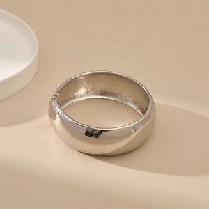 Macro view of a polished silver metal bangle featuring a smooth finish and a hinge closure