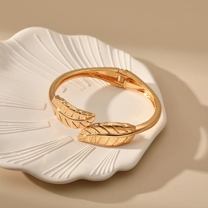 Detail of a golden leaf-shaped open cuff bracelet resting on a white shell tray