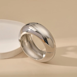 Detailed view of wide polished silver metal bangle with a sleek hinge closure mechanism
