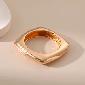 Close-up of polished gold square bangle showing the spring hinge opening mechanism