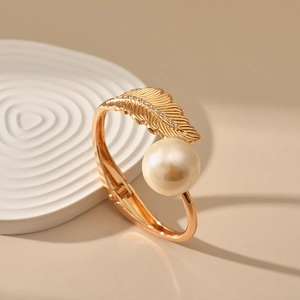 Detail of leaf-shaped gold bracelet featuring sparkling crystals and a large cream pearl