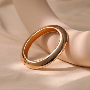 Detailed close-up of a high-polish gold oval bangle with a functional hinge clasp