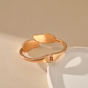Detail of rose gold hinged cuff bracelet with textured leaf ends on a white tray