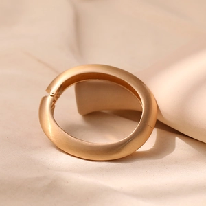 Detail of a minimalist gold bangle with brushed metal finish on soft beige silk background