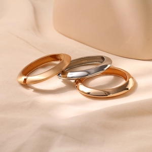 Detail of three chunky metal bangles in gold and silver finishes on beige fabric