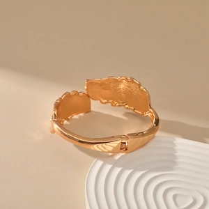 Close-up of golden leaf bangle with spring hinge mechanism on a white display