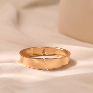 Close-up of golden polished bangle featuring a unique cross-over design and hinge closure
